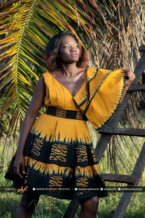 Robe batik couleur or et noire, évasée à double ovale superposées, manches asymétriques à volants, avec ceinture brodée.