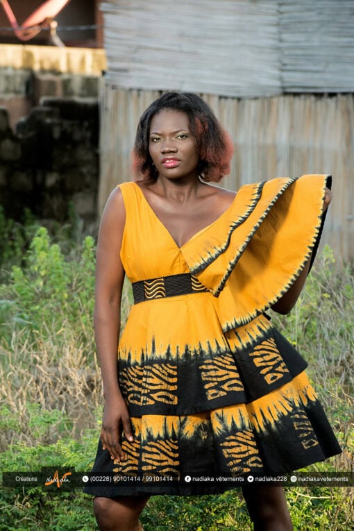 Robe batik couleur or et noire, évasée à double ovale superposées, manches asymétriques à volants, avec ceinture brodée.