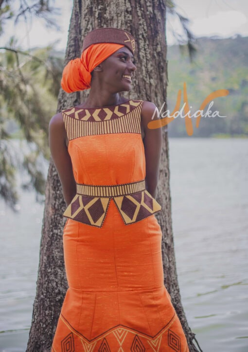 Robe longue brodée, en pagne tissé orange à brillantine or, Avec ceinture large brodée. Foulard et chapeau brodé assortis.