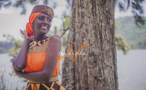Robe longue brodée, en pagne tissé orange à brillantine or, Avec ceinture large brodée. Foulard et chapeau brodé assortis.