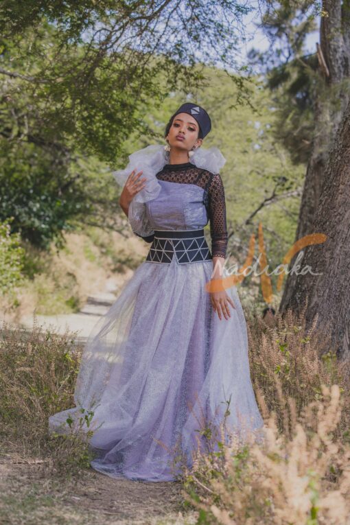 Robe longue, en pagne tissé couleur argentée, à brillantine argent, mix tulles brillant argent et dentelles noires. Avec ceinture large brodée et froufrous. Foulard et chapeau brodé assortis.