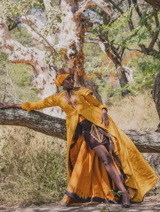 Robe longue brodée à traîne, en pagne tissé couleur moutarde à brillantine or. Jupe en tissu batik marron Foulard et chapeau brodé assortis.