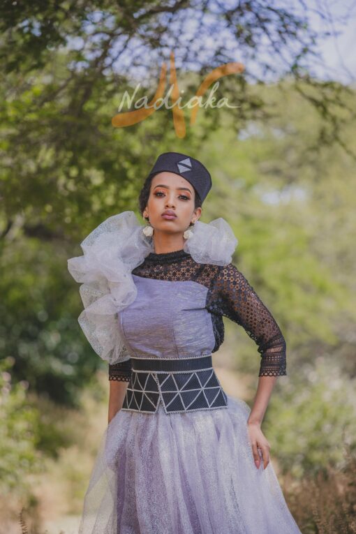 Robe longue, en pagne tissé couleur argentée, à brillantine argent, mix tulles brillant argent et dentelles noires. Avec ceinture large brodée et froufrous. Foulard et chapeau brodé assortis.