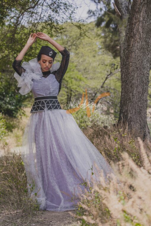 Robe longue, en pagne tissé couleur argentée, à brillantine argent, mix tulles brillant argent et dentelles noires. Avec ceinture large brodée et froufrous. Foulard et chapeau brodé assortis.