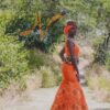 Robe longue brodée, en pagne tissé orange à brillantine or, Avec ceinture large brodée. Foulard et chapeau brodé assortis.