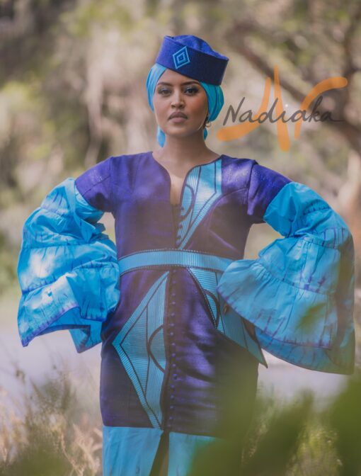 Robe longue volantée, brodée, en pagne tissé à brillantine, mix tissu batik couleur bleue turquoise et bleu. Avec ceinture large asymétrique brodée. Foulard et chapeau brodé assortis.