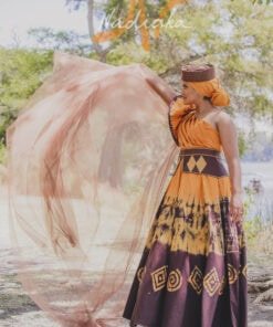 Robe longue, haut drapé, en tissu batik couleur moutarde et marron. Avec ceinture large brodée et tulles traîne brillant marron. Foulard et chapeau brodé assortis.