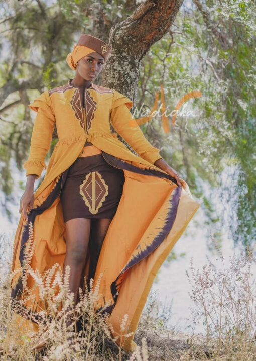 Robe longue brodée à traîne, en pagne tissé couleur moutarde à brillantine or. Jupe en tissu batik marron Foulard et chapeau brodé assortis.