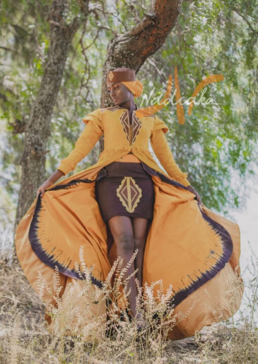 Robe longue brodée à traîne, en pagne tissé couleur moutarde à brillantine or. Jupe en tissu batik marron Foulard et chapeau brodé assortis.