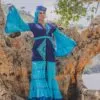 Robe longue volantée, brodée, en pagne tissé à brillantine, mix tissu batik couleur bleue turquoise et bleu. Avec ceinture large asymétrique brodée. Foulard et chapeau brodé assortis.