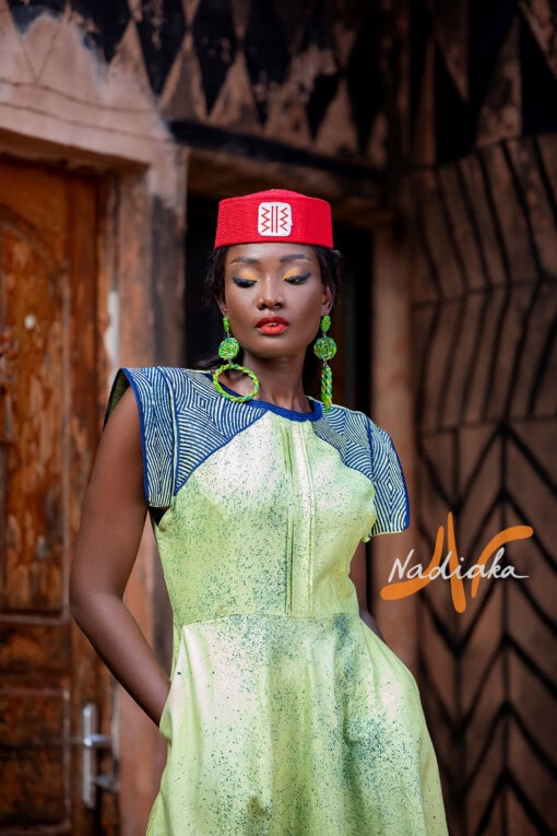 Robe longue de couleur verte, brodée en teinture à jets , ovale de la taille jusqu'au bas assortie d'un chapeau Apéto rouge à motif blanc