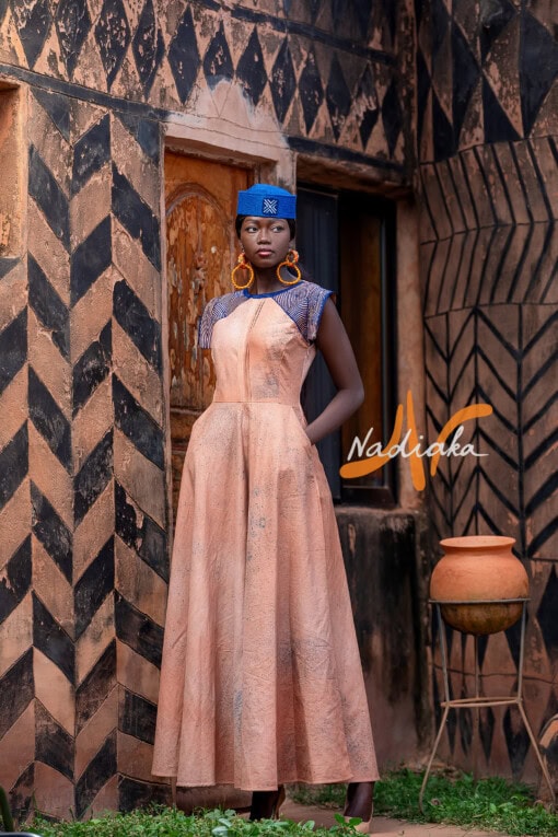 Robe longue ovale en teinture à jets nude assortie avec un chapeau apéto bleu et des boucles d'oreilles en pailles