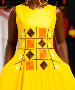 Longue robe brodé de couleur jaune moutarde sans manches en tissu coton woodin avec des broderies à l'avant. La robe est agrémentée de fentes en bas sur chaque coté.